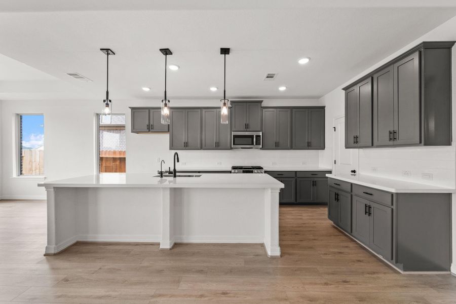 This light and bright kitchen features a large quartz island, white cabinets, a large sink overlooking your family room, recessed lighting, and beautiful backsplash.
