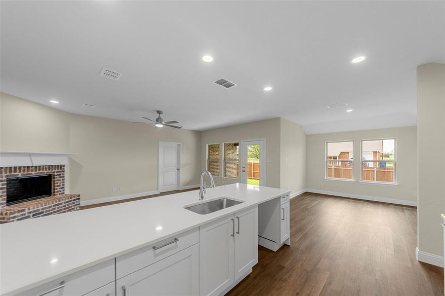 Expansive kitchen island with a built-in sink and white cabinetry, wood-finish flooring, recessed lighting, a brick fireplace with a white mantel, and multiple large windows