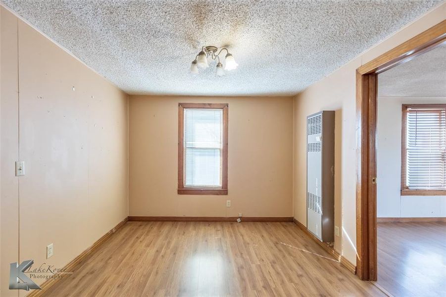 Spare room featuring light wood-type flooring, a heating unit, plenty of natural light, and a textured ceiling Spare room featuring light wood-type flooring, a heating unit, plenty of natural light, and a textured ceiling