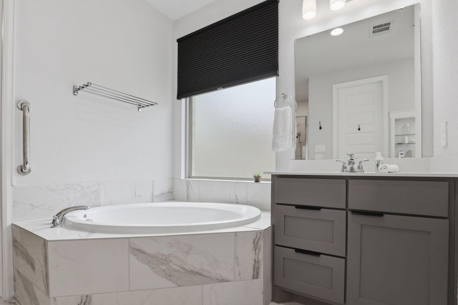 A detailed view of the deep soaking tub surrounded by elegant marble-look tile.