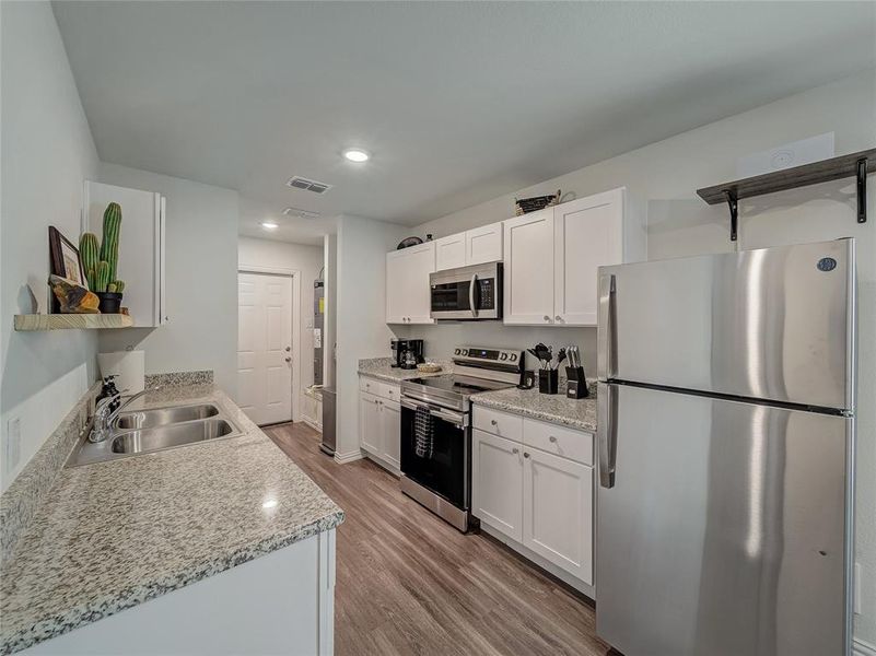 Kitchen with stainless steel appliances, light wood-style flooring, white cabinetry, open shelves, and recessed lighting
