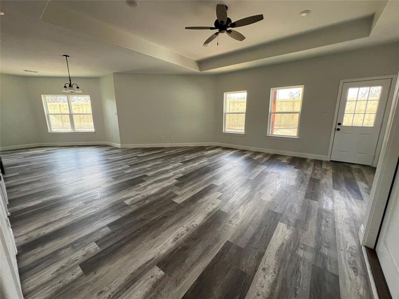 Unfurnished living room featuring dark wood-style floors, ceiling fan with notable chandelier, a raised ceiling, and baseboards