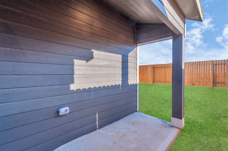 Enjoy the outdoors in comfort with this covered patio area, offering a serene spot for morning coffee or evening relaxation. The cozy space is perfect for setting up a small seating area or a BBQ grill. Surrounded by lush green grass and a sturdy wooden fence, this area provides both privacy and the perfect outdoor extension to your living space. **This image is from another Saratoga Home - Clover floorplan.**