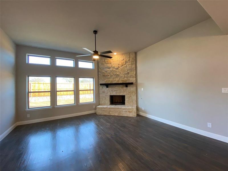 Rich handscraped Aged Barrell hardwood floors, a wall of windows, gas stone fireplace, and ceiling fan in this family room