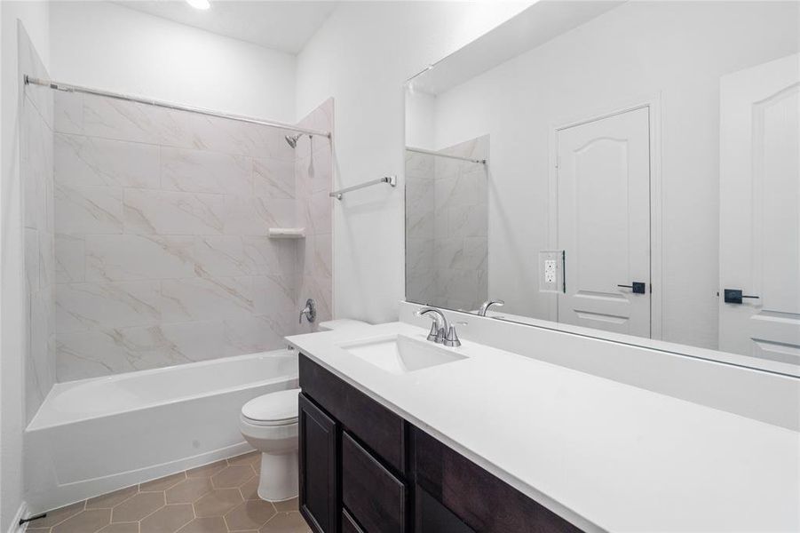 Secondary bath features tile flooring, bath/shower combo with tile surround, stained wood cabinets, beautiful light countertops, mirror, sleek fixtures and modern finishes.