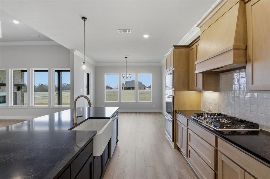 Kitchen with two tone color scheme, dark stone countertops, light wood-style floors, tasteful backsplash, and crown molding