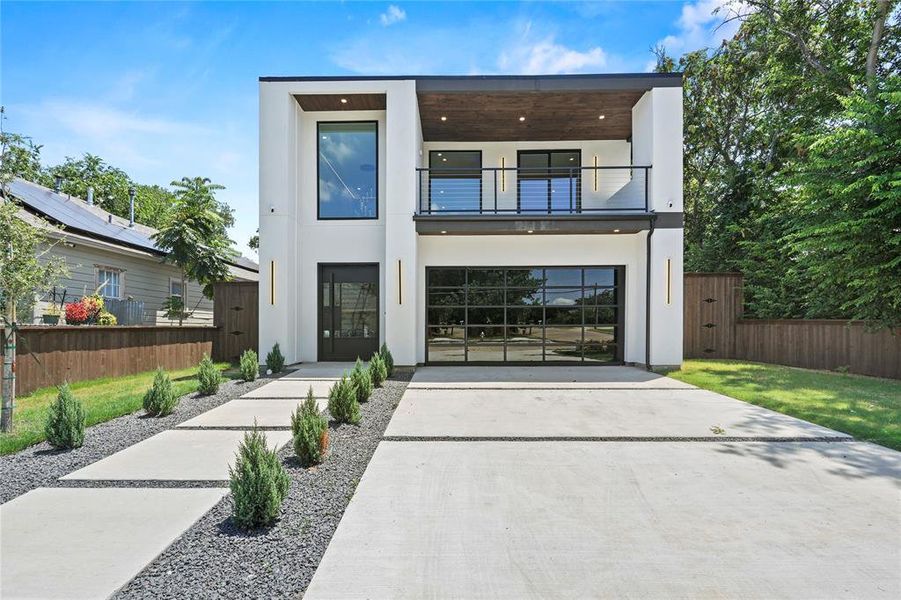 Contemporary home featuring a balcony, concrete driveway, stucco siding, an attached garage, and a gate