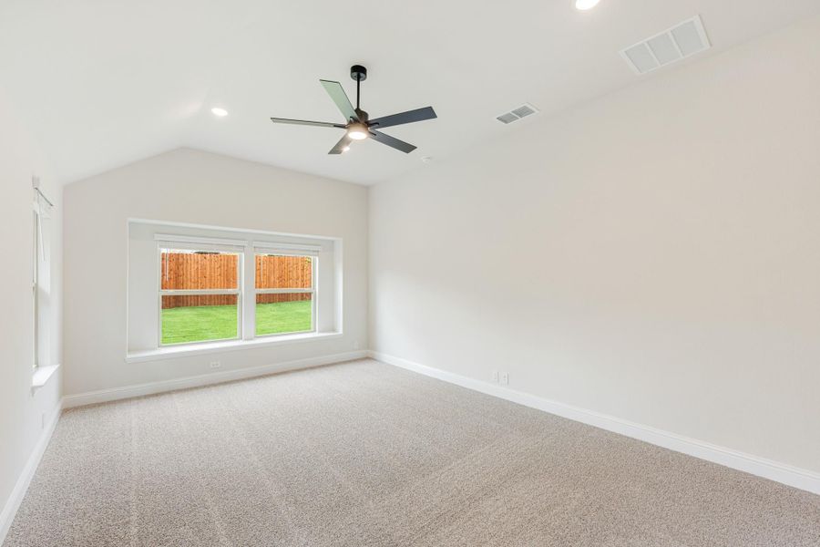 Empty bedroom with vaulted ceiling, ceiling fan, carpet flooring, and backyard-facing window Empty bedroom with vaulted ceiling, ceiling fan, carpet flooring, and backyard-facing window