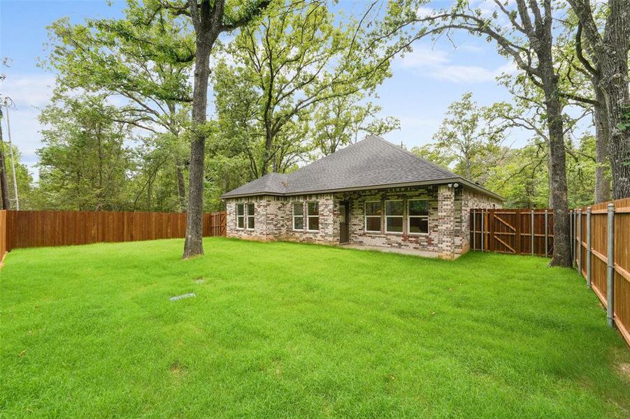 Expansive rear yard featuring a manicured lawn, full privacy fencing, and mature trees Expansive rear yard featuring a manicured lawn, full privacy fencing, and mature trees