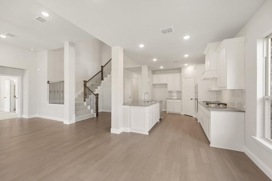 Open-concept kitchen with white cabinets, center island, and hardwood floors, with staircase visible in background.