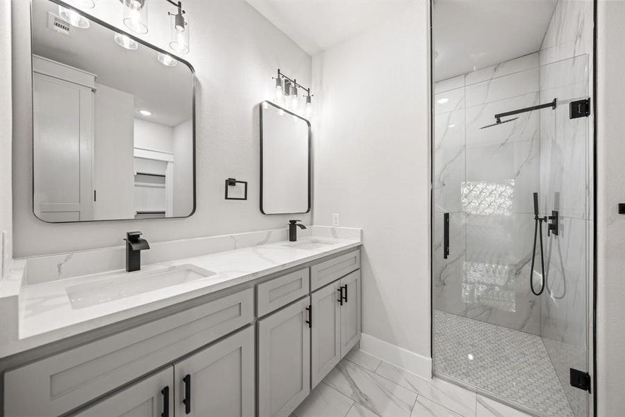 Full bath featuring a marble finish shower, double vanity, and light marble finish flooring
