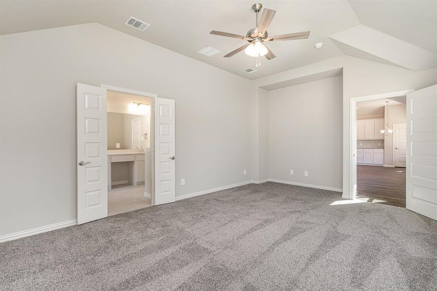 Unfurnished bedroom with ceiling fan, light colored carpet, ensuite bath, and vaulted ceiling