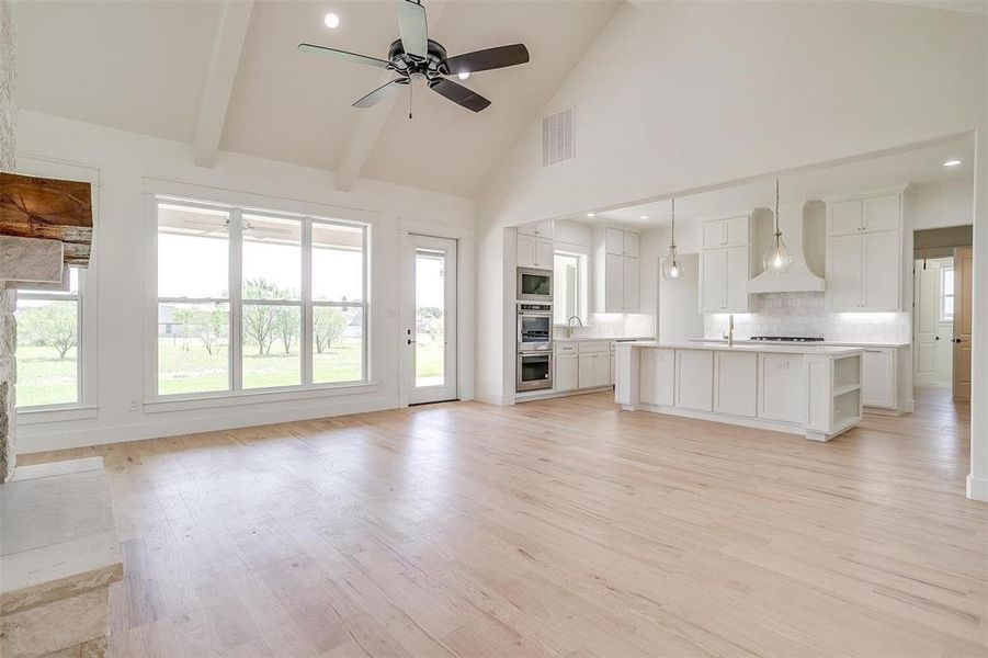 Unfurnished living room with a ceiling fan, high vaulted ceiling, light wood-style flooring, a sink, and recessed lighting