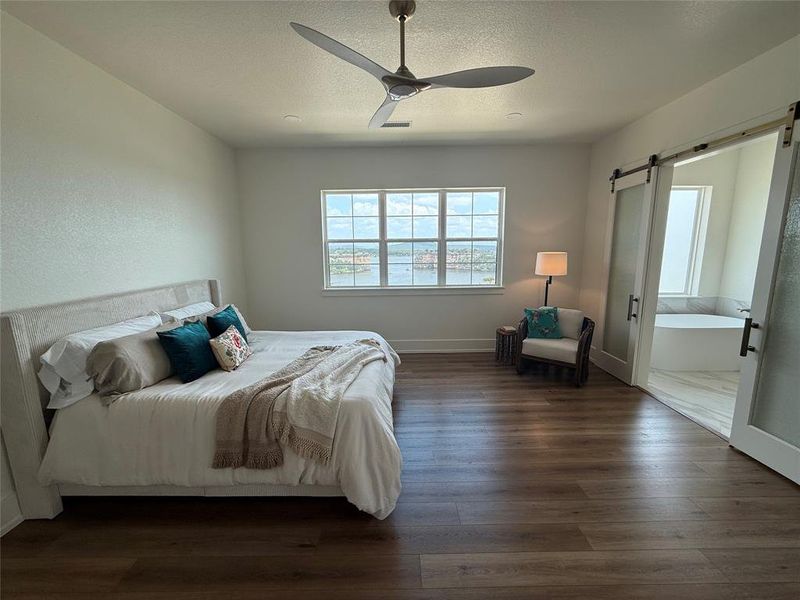 Bedroom featuring a barn door, dark wood-type flooring, ceiling fan, and a textured ceiling Bedroom featuring a barn door, dark wood-type flooring, ceiling fan, and a textured ceiling