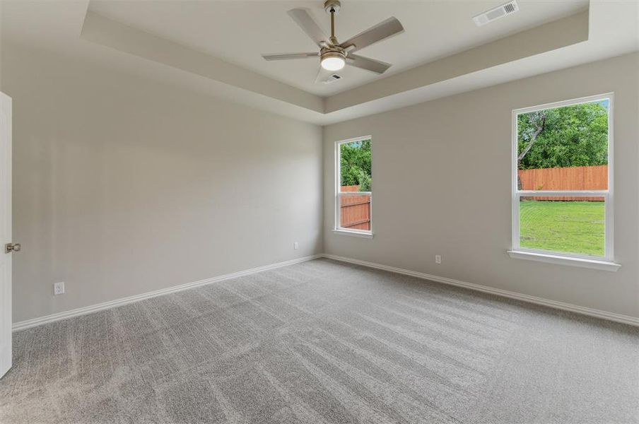 Spacious room featuring tray ceiling, flush-mount ceiling fan with integrated lighting, soft gray wall paint, and light gray patterned carpeting