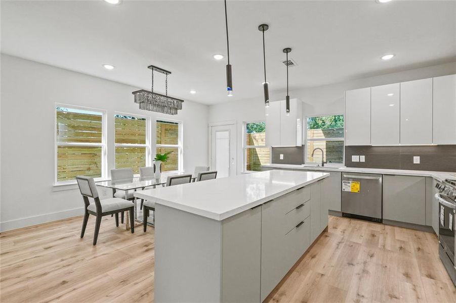 Kitchen featuring hanging light fixtures, light hardwood / wood-style flooring, white cabinetry, stainless steel appliances, and a center island