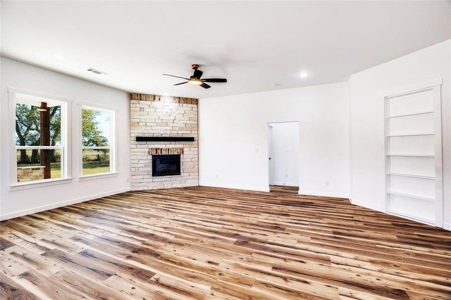 Unfurnished living room featuring a stone fireplace, built in features, wood finished floors, ceiling fan, and recessed lighting