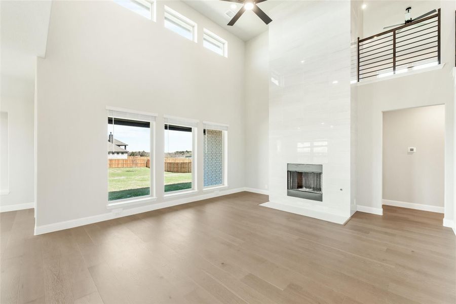Open living room with two-story ceiling, fireplace, hardwood floors, and large windows overlooking backyard Open living room with two-story ceiling, fireplace, hardwood floors, and large windows overlooking backyard