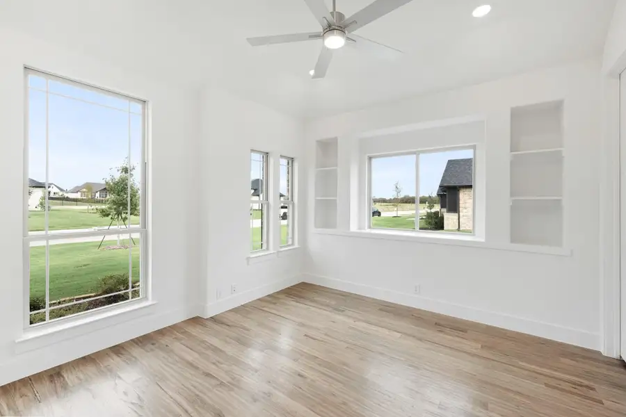 Empty room with hardwood floors, ceiling fan, large windows, and built-in wall shelves Empty room with hardwood floors, ceiling fan, large windows, and built-in wall shelves