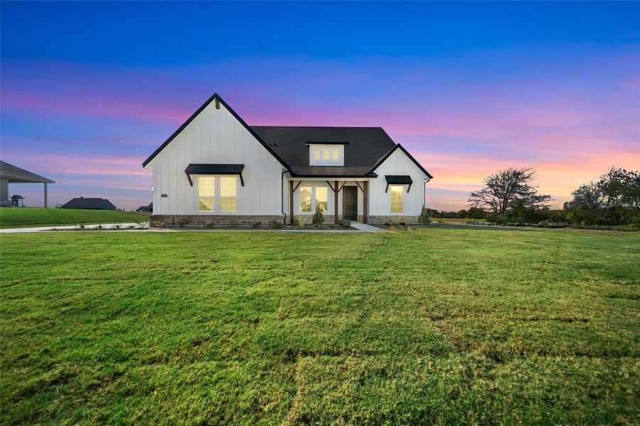 Modern farmhouse with a lawn, covered porch, and board and batten siding