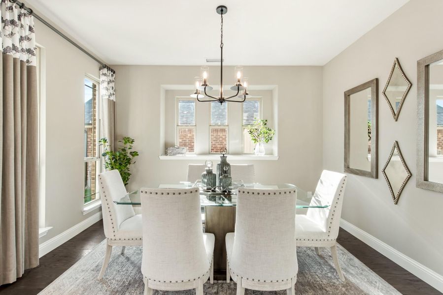 Dining room with glass table, six white upholstered chairs, and a chandelier overhead