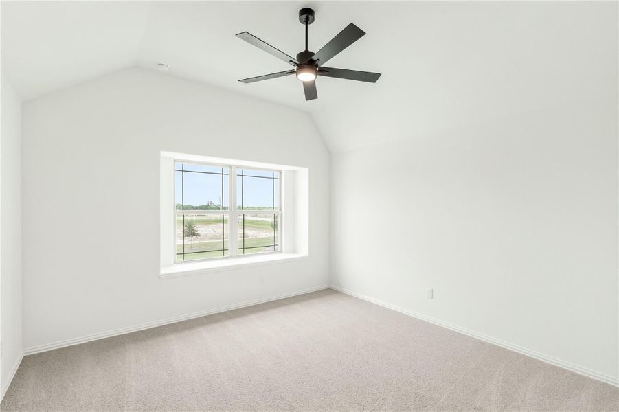 Empty bedroom with vaulted ceiling, ceiling fan, carpet flooring, and large window with outdoor view Empty bedroom with vaulted ceiling, ceiling fan, carpet flooring, and large window with outdoor view