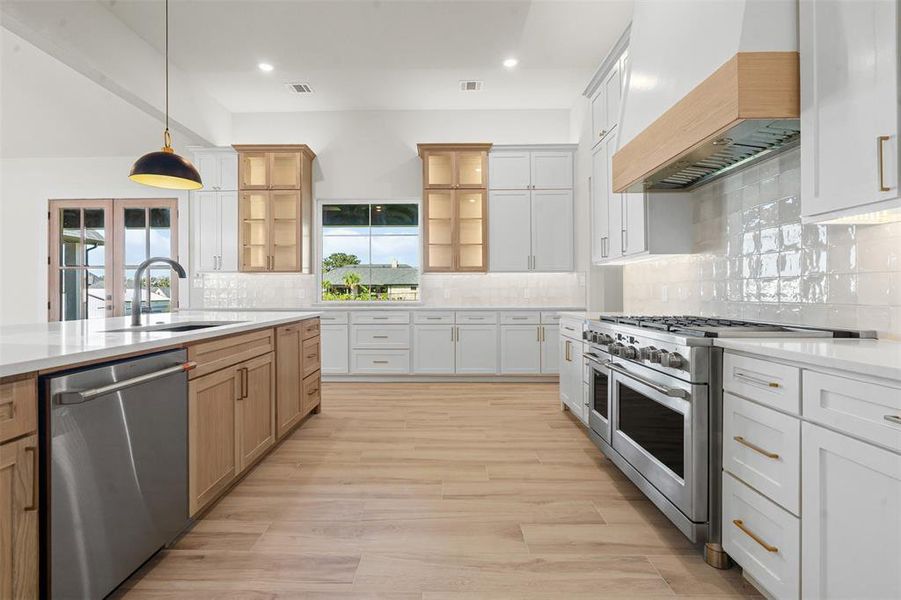 Kitchen with white cabinets, backsplash, premium range hood, stainless steel appliances, and pendant lighting Kitchen with white cabinets, backsplash, premium range hood, stainless steel appliances, and pendant lighting