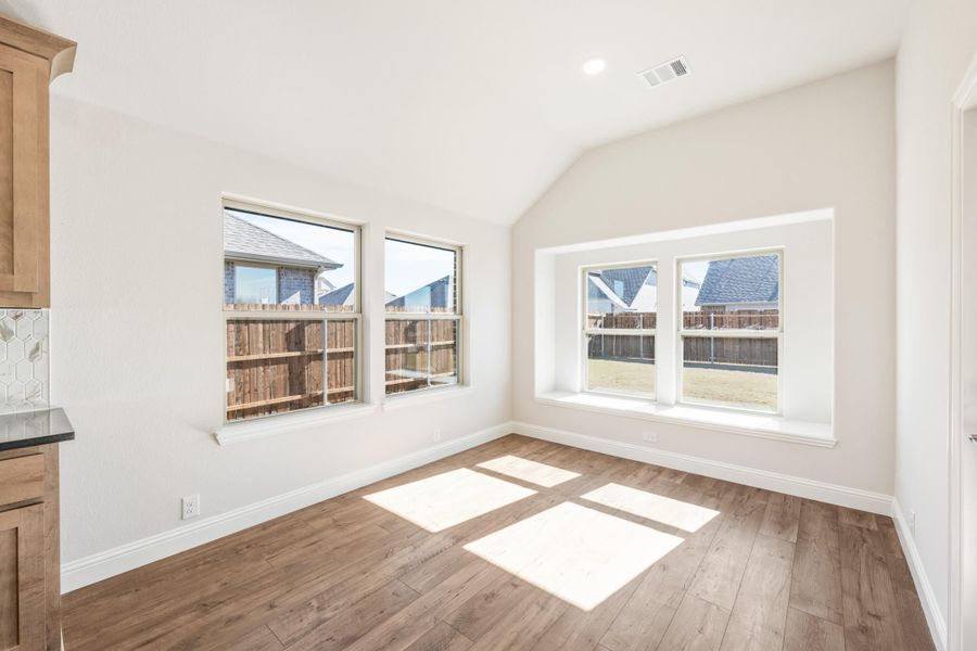 Empty dining or breakfast room with vaulted ceiling, hardwood floors, and large windows overlooking backyard fence Empty dining or breakfast room with vaulted ceiling, hardwood floors, and large windows overlooking backyard fence