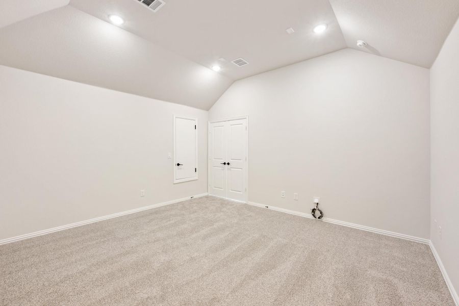 Empty bedroom with vaulted ceiling, carpet flooring, and double closet doors