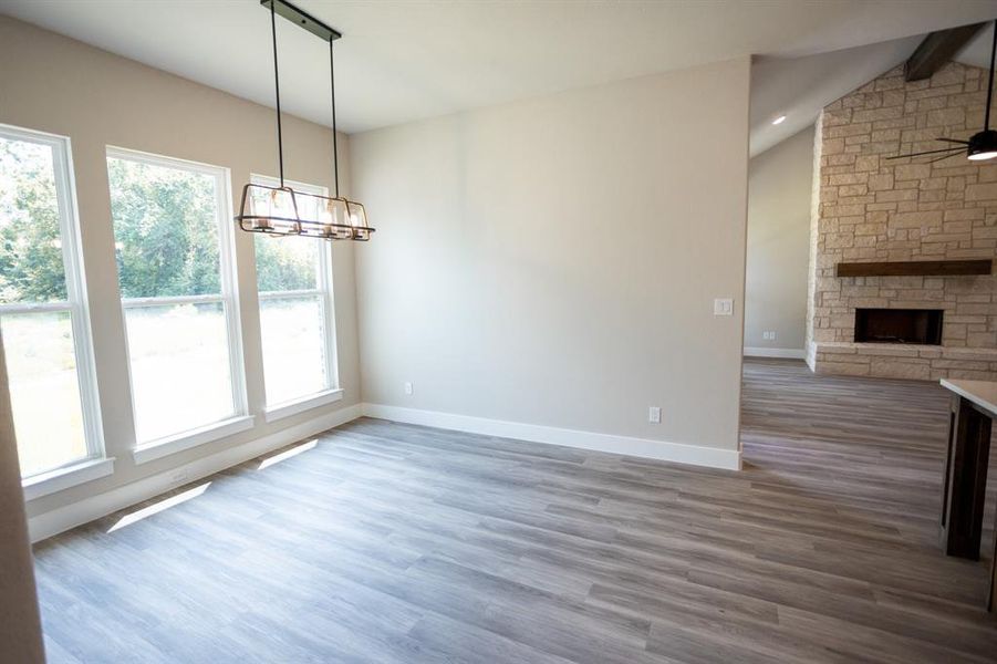 Unfurnished dining area with light wood-style floors, a stone fireplace, ceiling fan, and a chandelier Unfurnished dining area with light wood-style floors, a stone fireplace, ceiling fan, and a chandelier