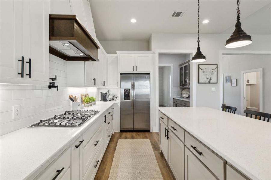 Contemporary kitchen featuring a gas cooktop, stainless steel refrigerator, white subway tile backsplash, white cabinetry with black hardware, and a large island with pendant lighting