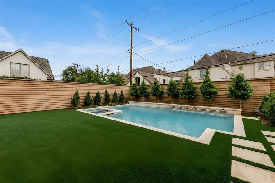 Backyard oasis featuring a rectangular swimming pool with integrated spa and water features, surrounded by a light-toned coping