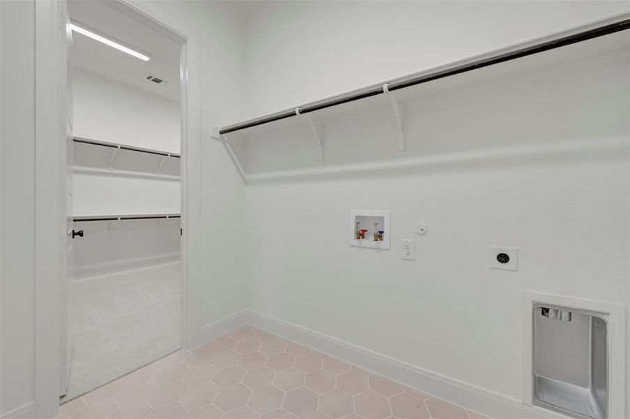 Laundry area featuring hexagonal tile flooring, a utility sink, and wall-mounted shelving with a clothing rod Laundry area featuring hexagonal tile flooring, a utility sink, and wall-mounted shelving with a clothing rod