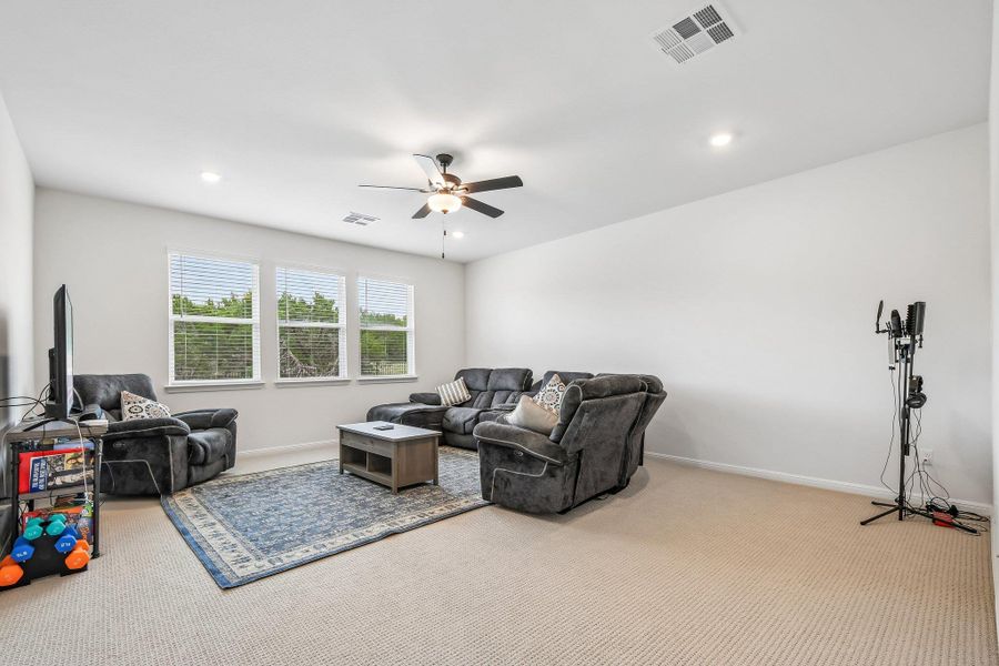 A comfortable living area features well-lit walls, ample windows, and a ceiling fan for optimal airflow.