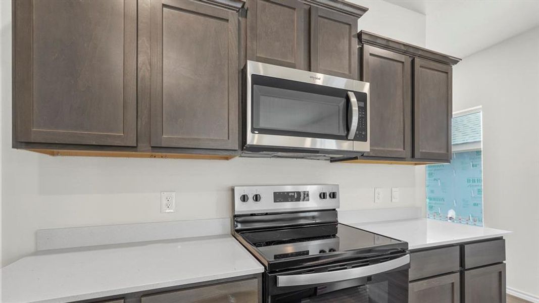 Kitchen featuring a stainless steel microwave, black electric range, gray shaker-style cabinetry, and light-colored countertops