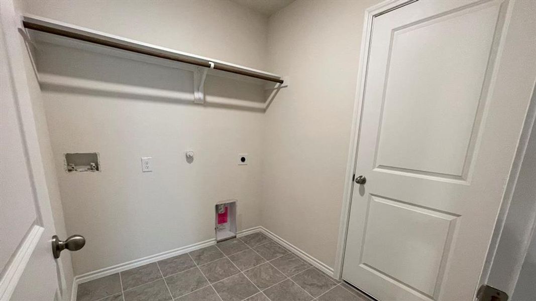 Utility area with tile flooring and a built-in shelving unit with hanging rod