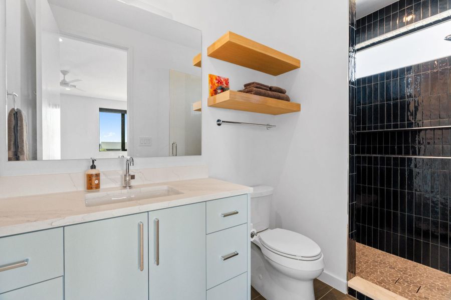 Bathroom featuring a light blue vanity with integrated sink, a large wall-mounted mirror, and floating wood shelves
