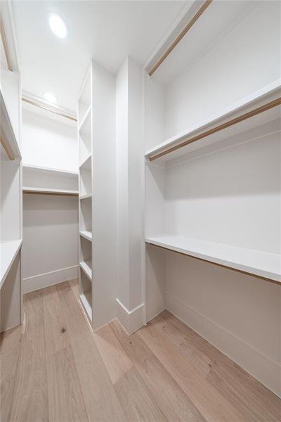 Walk-in closet featuring light wood-finish flooring, recessed lighting, white built-in shelving, and multiple hanging rods