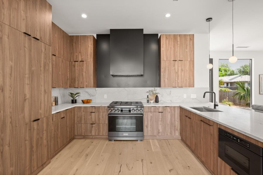 Kitchen featuring modern cabinets, light stone countertops, black appliances, light wood-style floors, and pendant lighting
