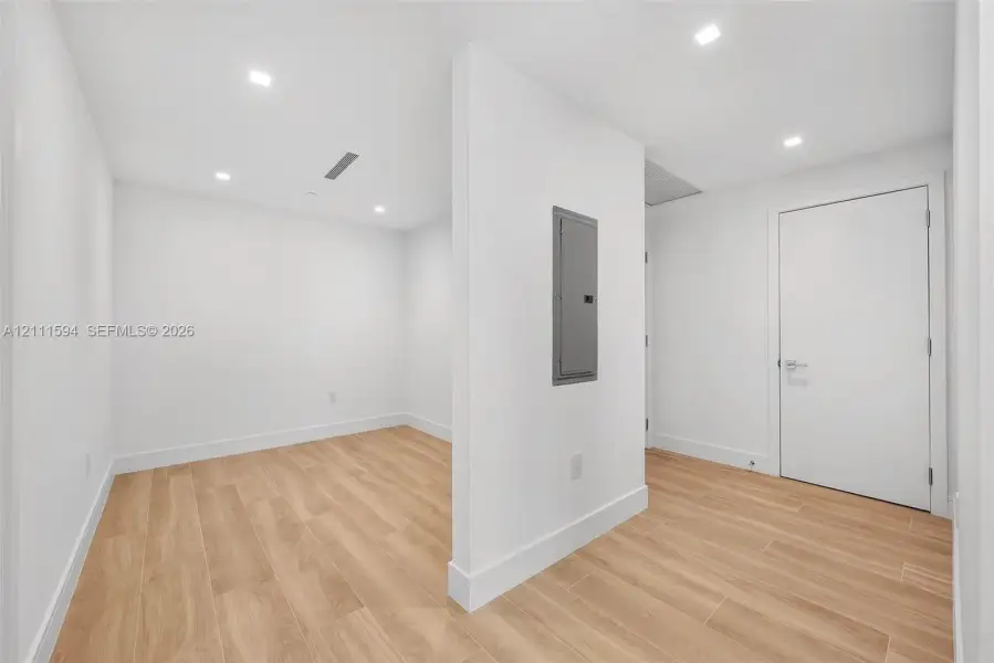 Interior room featuring wood-finish tile flooring, recessed ceiling lighting, and a central partition wall with an integrated electrical service panel Interior room featuring wood-finish tile flooring, recessed ceiling lighting, and a central partition wall with an integrated electrical service panel
