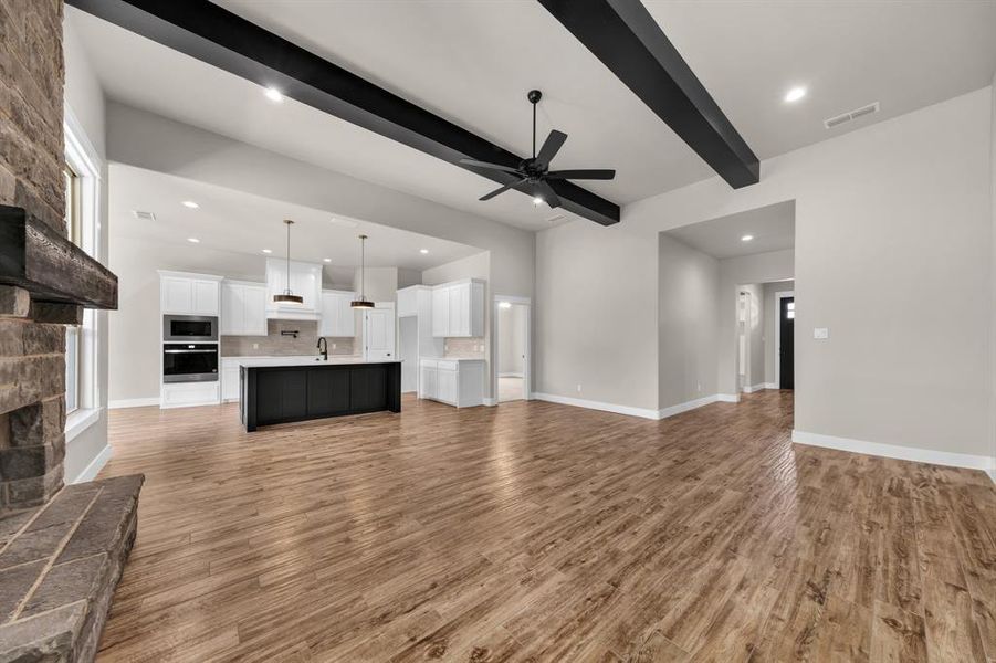 Unfurnished living room featuring beamed ceiling, hardwood / wood-style flooring, a stone fireplace, and ceiling fan