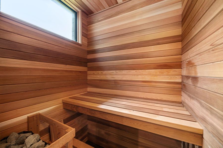 This photo shows a cozy sauna with beautifully finished wooden walls and benches, featuring a window for natural light and a stone heater for an authentic sauna experience. This photo shows a cozy sauna with beautifully finished wooden walls and benches, featuring a window for natural light and a stone heater for an authentic sauna experience.