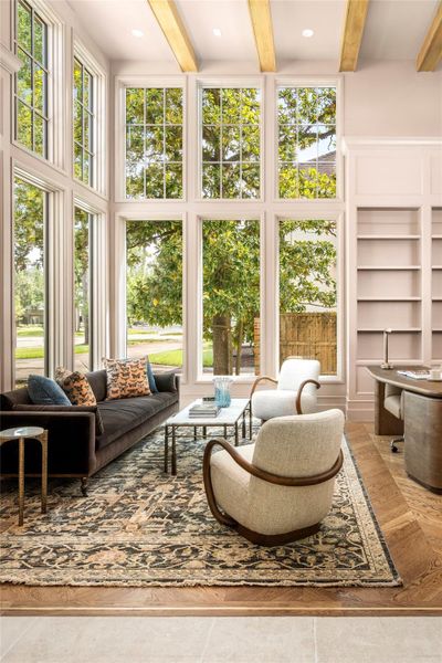 Flooded with natural light, the library is framed by soaring front-facing windows and custom built-in cabinetry, with full-height paneled wainscoting and warm alder ceiling beams adding architectural depth. White oak chevron flooring with a brass inlay border brings a refined finishing touch. Flooded with natural light, the library is framed by soaring front-facing windows and custom built-in cabinetry, with full-height paneled wainscoting and warm alder ceiling beams adding architectural depth. White oak chevron flooring with a brass inlay border brings a refined finishing touch.