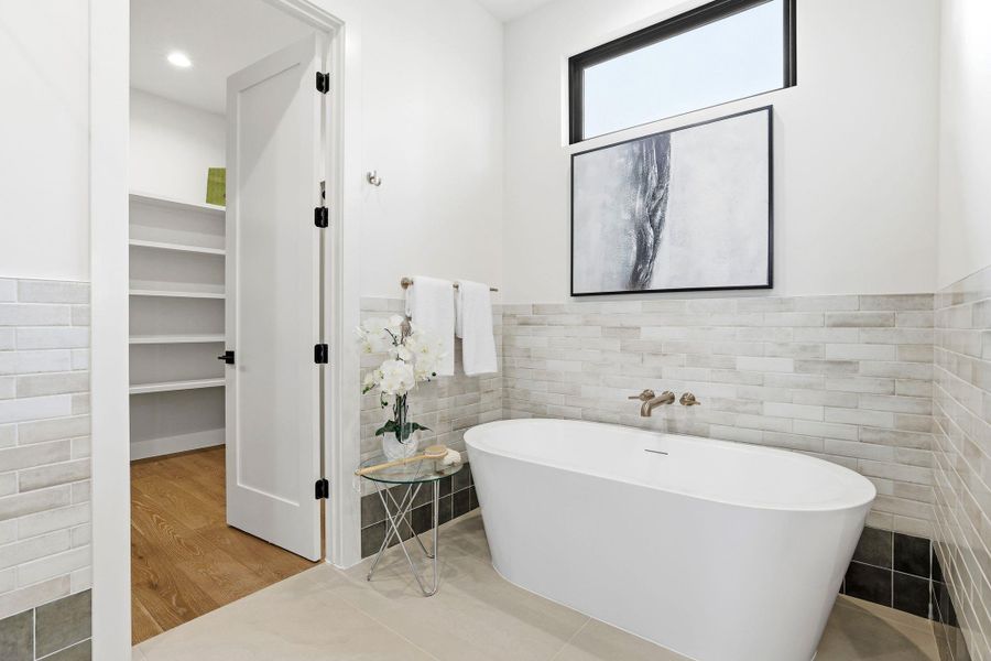 Bathroom featuring a soaking tub, wainscoting, tile walls, a walk in closet, and light tile patterned flooring Bathroom featuring a soaking tub, wainscoting, tile walls, a walk in closet, and light tile patterned flooring