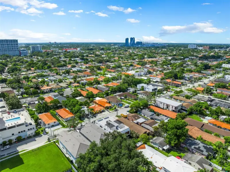 Aerial perspective featuring an established urban residential grid, mature canopy trees, and high-rise metropolitan skyline in the distance Aerial perspective featuring an established urban residential grid, mature canopy trees, and high-rise metropolitan skyline in the distance