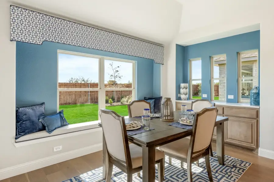 Dining area with wood table, four chairs, window seat, and blue accent walls overlooking a backyard