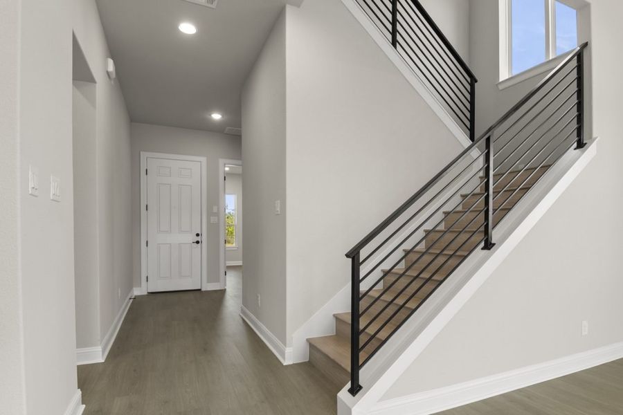 Image of a two story home foyer with wooden flooring and stairs with a black railing and light grey painted walls with white trim