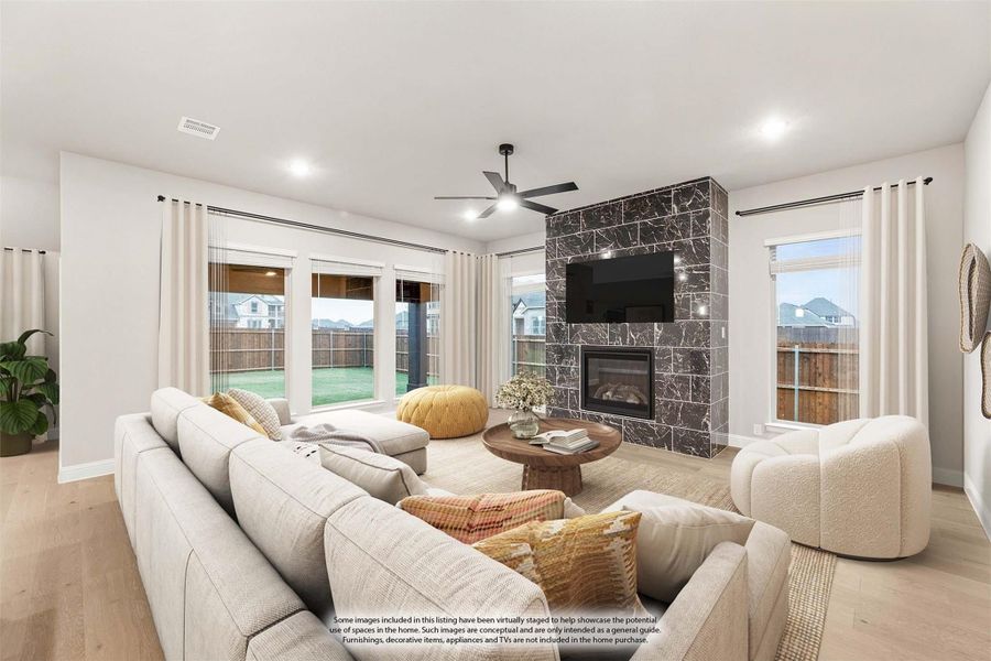 Living room with dark stone fireplace, ceiling fan, sectional sofa, and large windows with backyard view