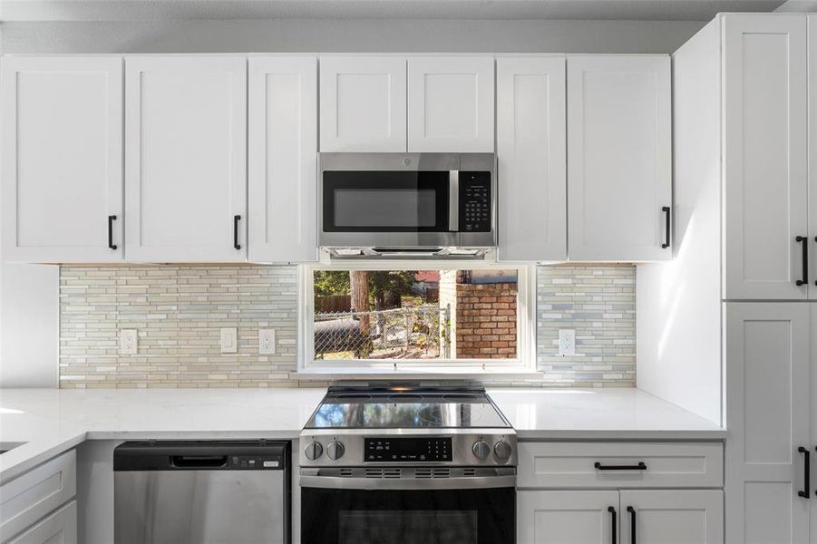 Kitchen featuring stainless steel appliances, white cabinets, and light stone countertops