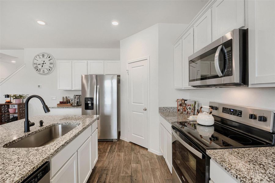 Kitchen featuring wood-finish flooring, white cabinetry, granite countertops, stainless steel appliances, and recessed lighting Kitchen featuring wood-finish flooring, white cabinetry, granite countertops, stainless steel appliances, and recessed lighting